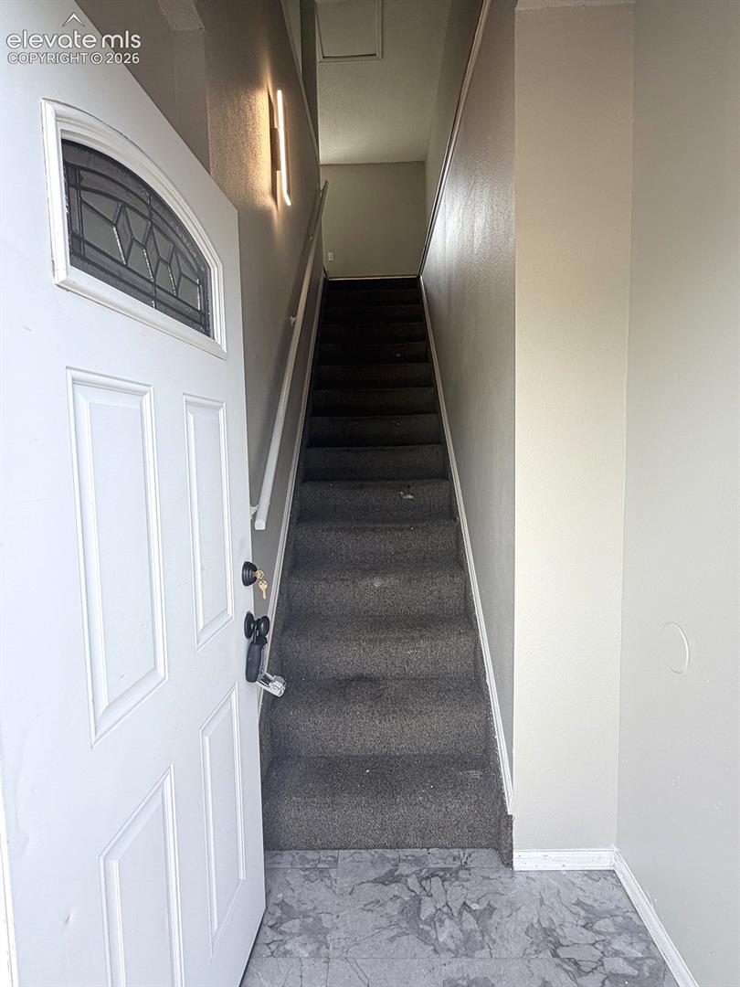 Entryway featuring a white paneled door with decorative glass, gray patterned flooring, and a carpeted staircase with a modern wall sconce
