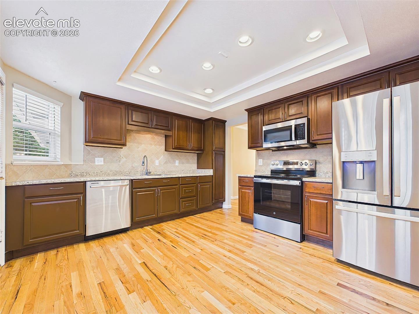 Kitchen – Updated kitchen featuring rich wood cabinetry, stainless steel appliances, tile backsplash, recessed lighting, and beautiful hardwood flooring.