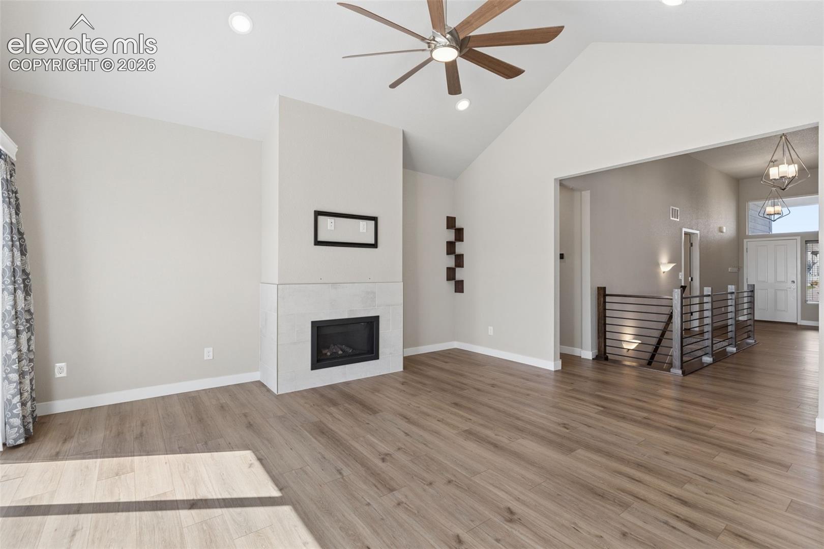 Vaulted ceiling, stone-surround fireplace, wood-finish flooring, ceiling fan, and staircase with metal railings