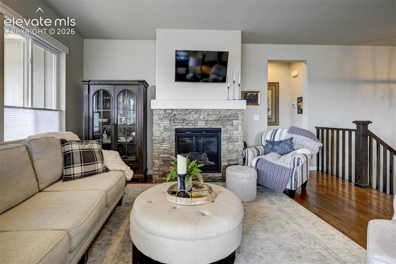 Stone-clad fireplace with a white mantel, hardwood flooring, and a dark wood banister