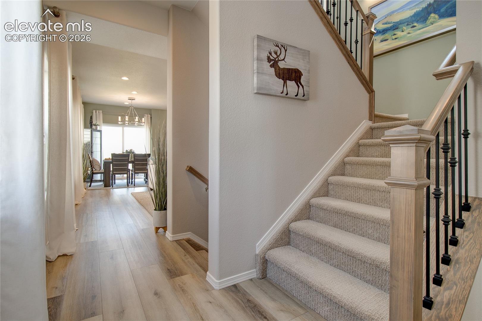 Foyer featuring wood-finish flooring, staircase with neutral carpeting, stained wooden handrails, and matte black metal balusters