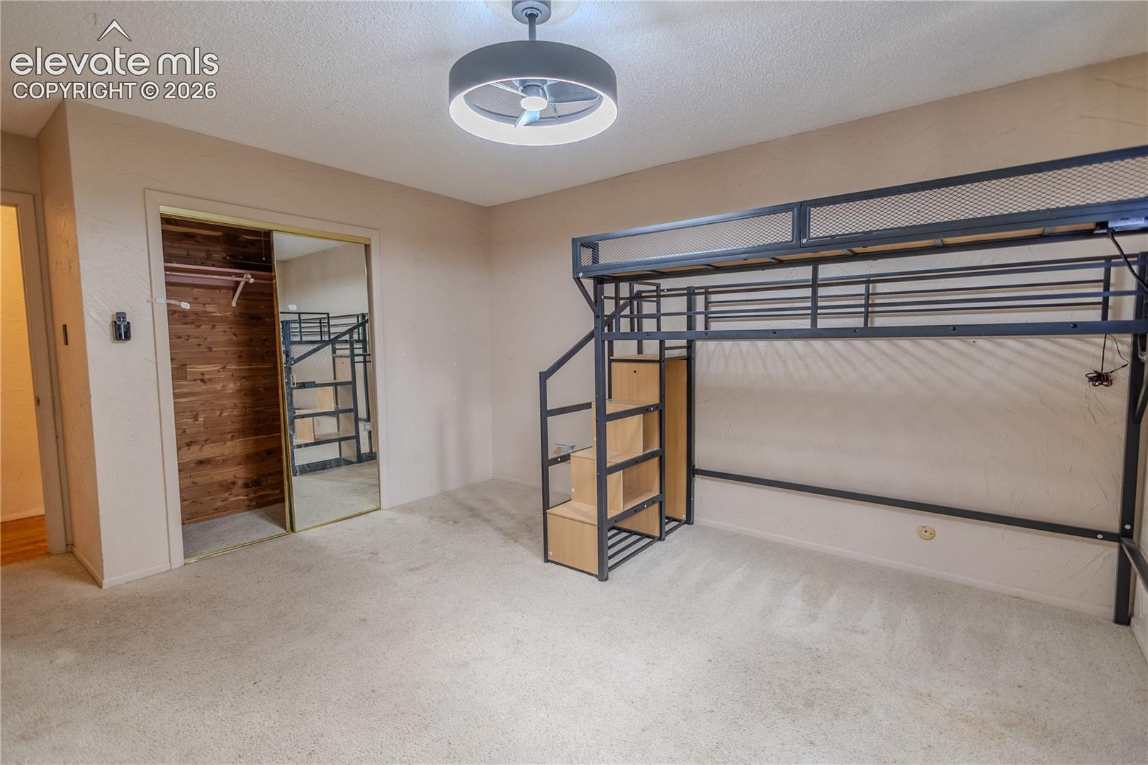 Closet featuring mirrored sliding doors and wood-plank interior wall paneling, complemented by a contemporary circular flush-mount ceiling fixture with integrated fan
