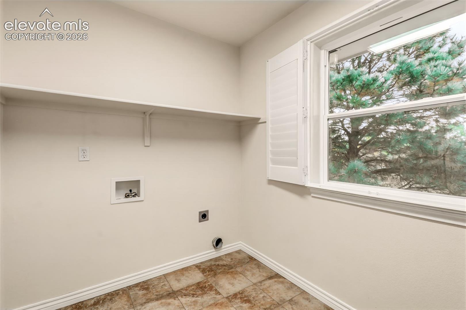 Utility area featuring tile flooring, a wall-mounted shelf, and a window with plantation-style shutters