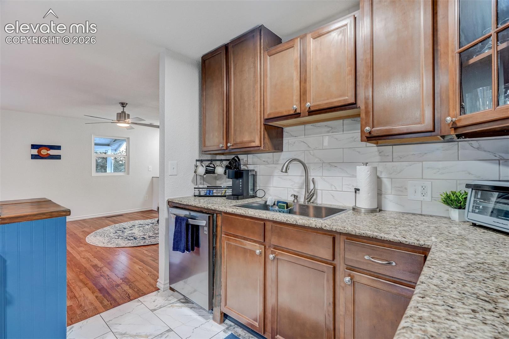 Kitchen featuring wood-finish cabinetry, light-toned countertop, subway tile backsplash, and stainless steel sink