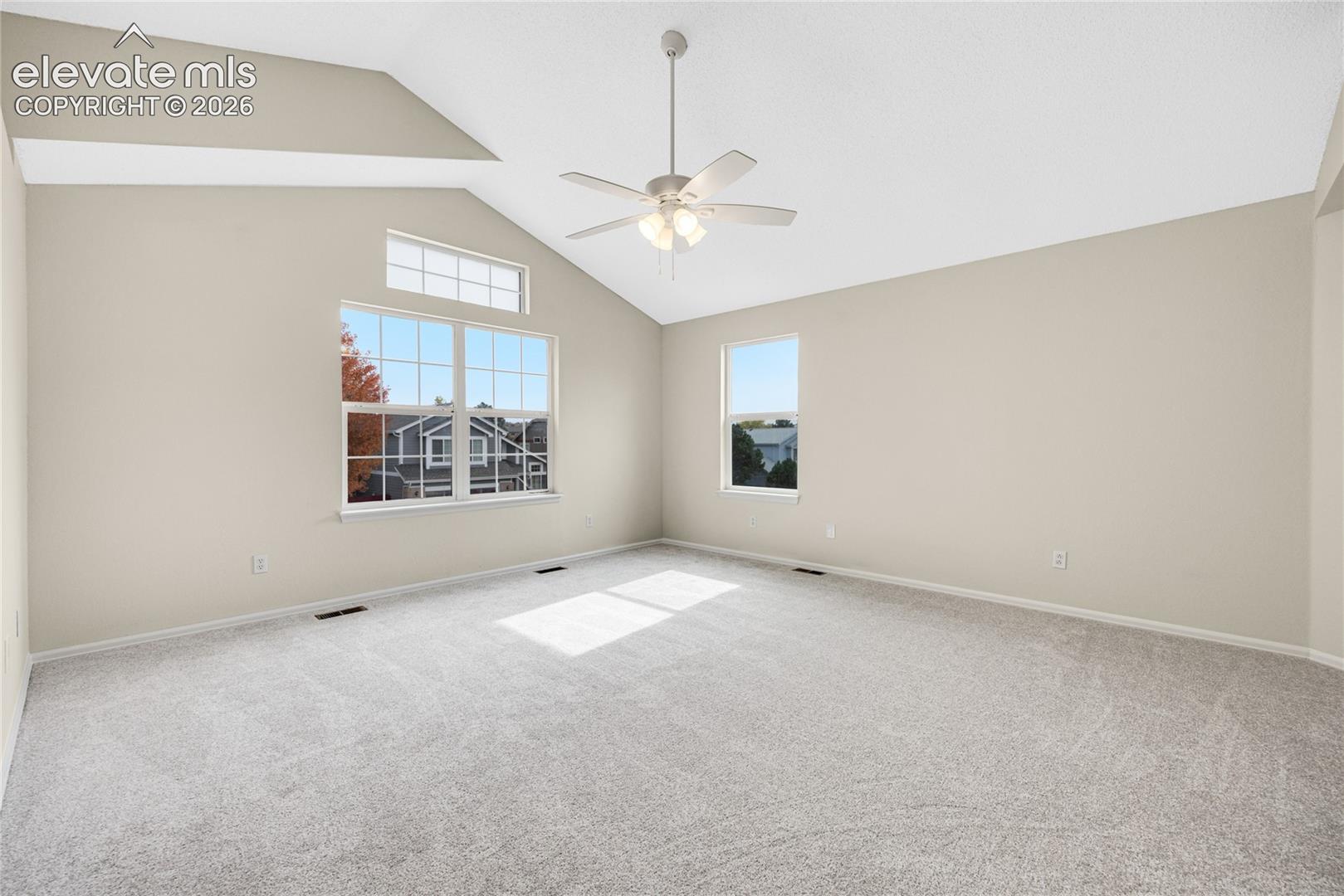 Vaulted ceiling, neutral wall tones, carpeted flooring, multi-pane windows, and a central ceiling fan with integrated lighting