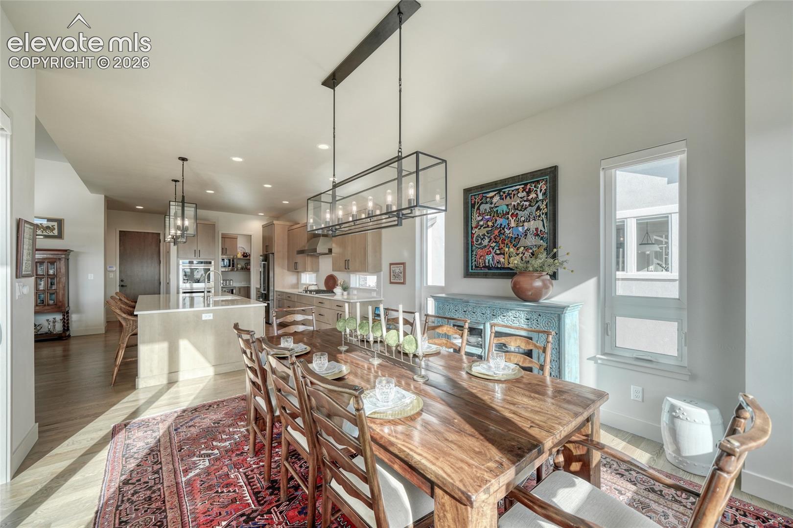 Open-concept dining area featuring recessed lighting, a linear metal chandelier, wood-finish flooring, and cabinetry with stone countertops