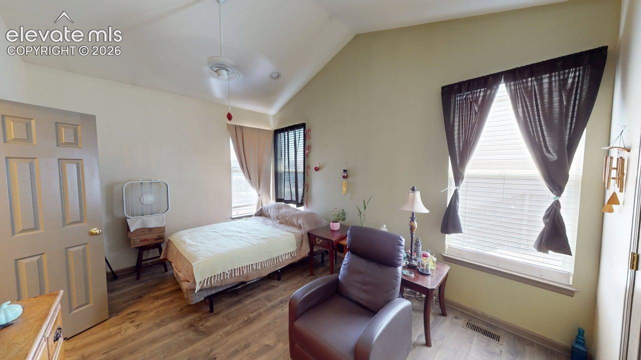 Vaulted ceiling room featuring wood-finish flooring, two windows with blinds, a paneled door, and a ceiling fan with integrated lighting