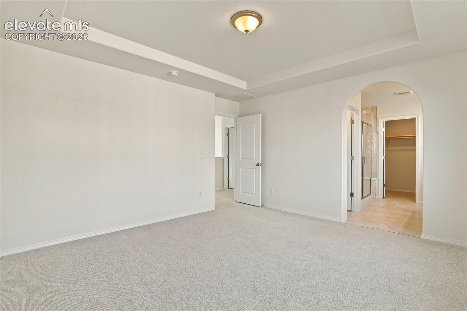 Tray ceiling, arched doorway, and neutral wall-to-wall carpeting