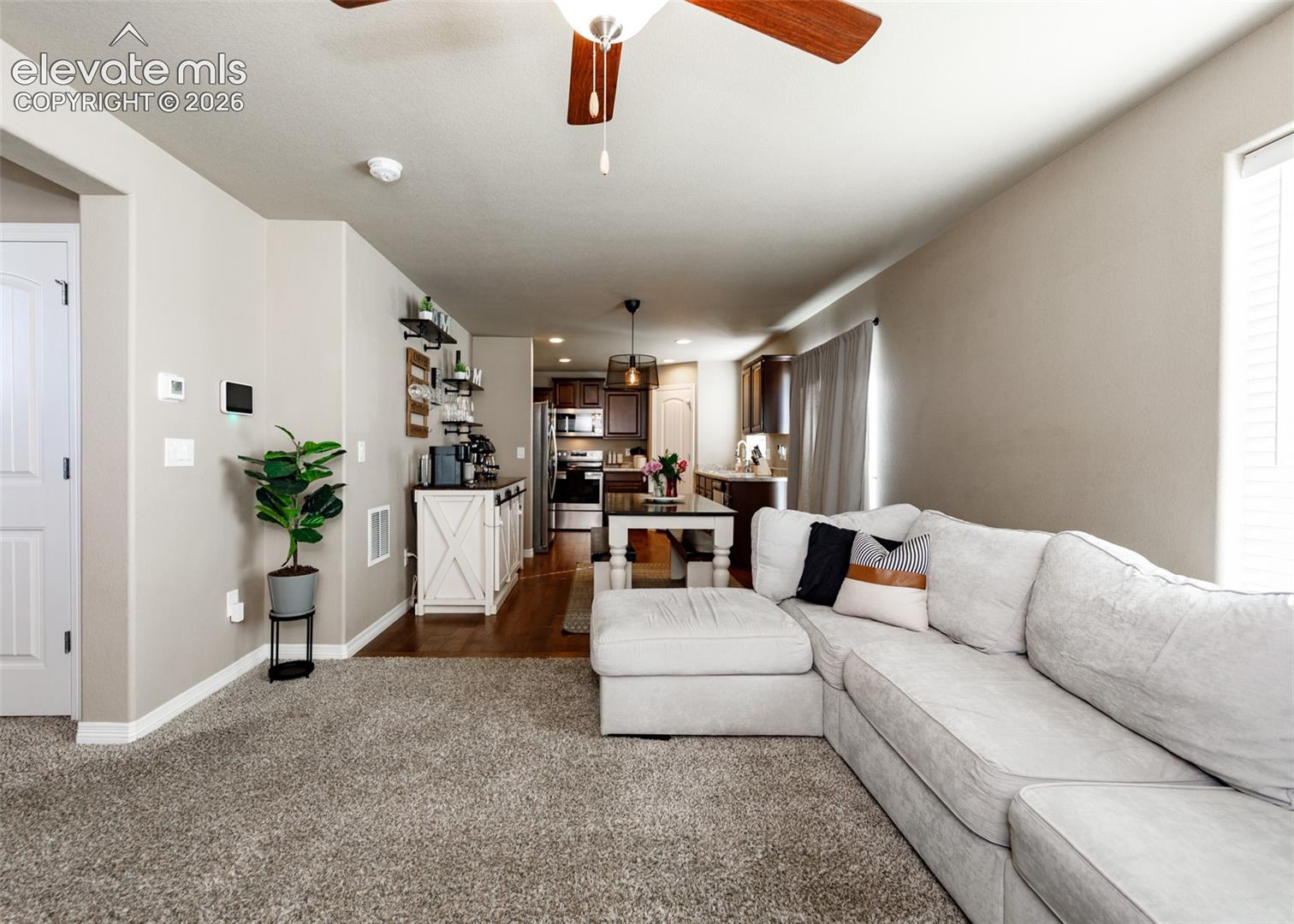 Open-concept interior featuring neutral wall tones, wood-finish flooring, a ceiling fan with integrated lighting, and a pendant fixture over the dining area