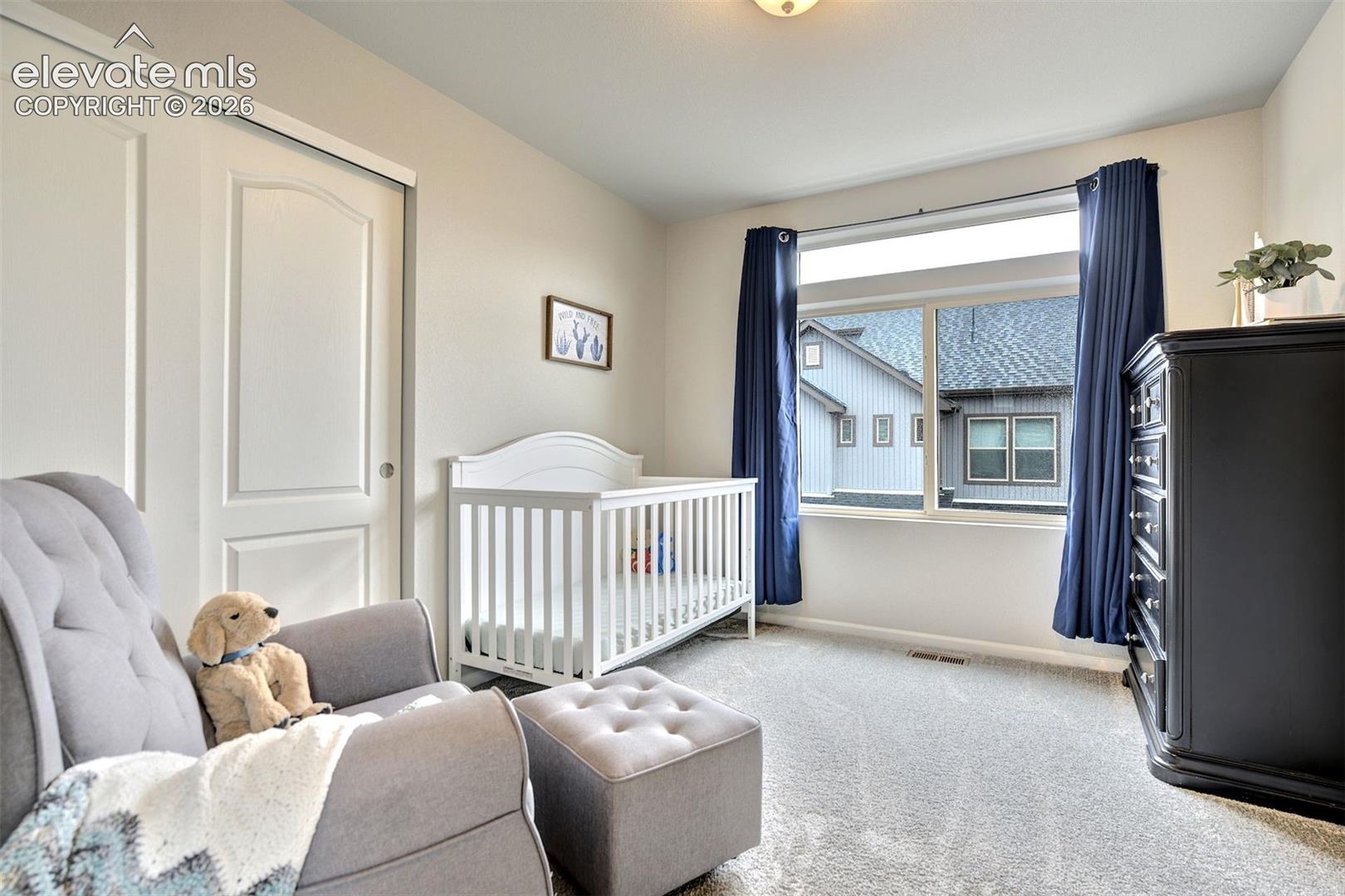 Neutral-toned bedroom featuring wall-to-wall carpeting, a large window with a transom light, and a double-door closet with arched paneling