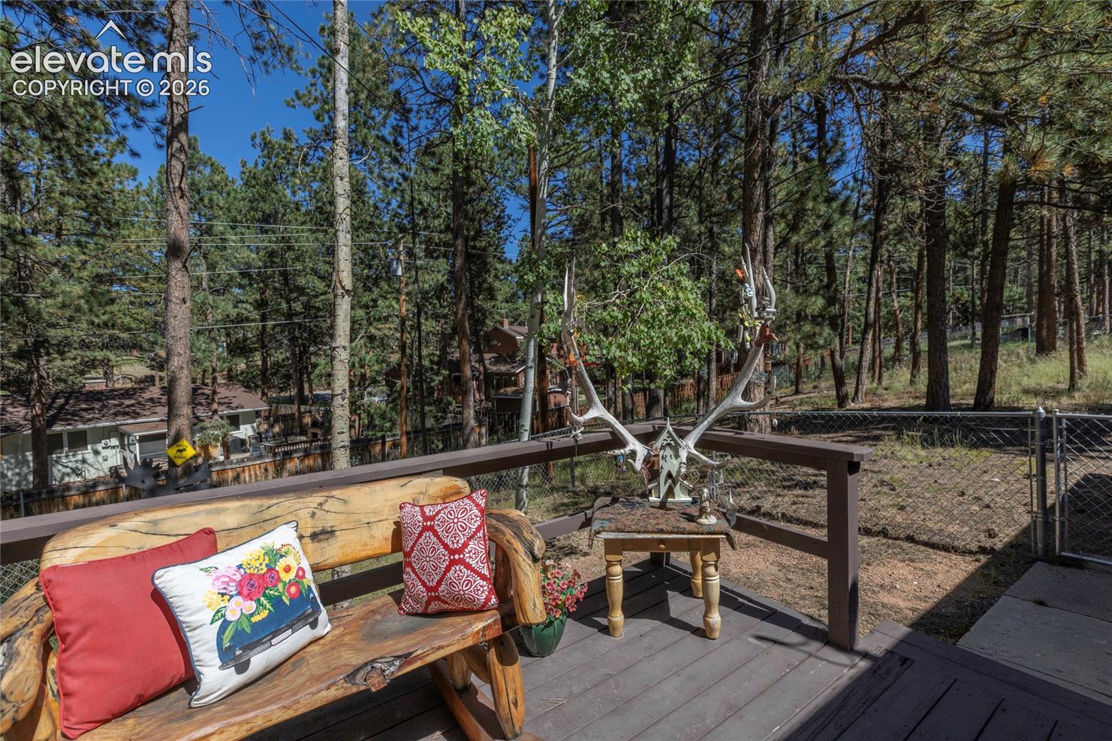 Elevated deck with wood-finish flooring and a natural wood bench, surrounded by mature trees