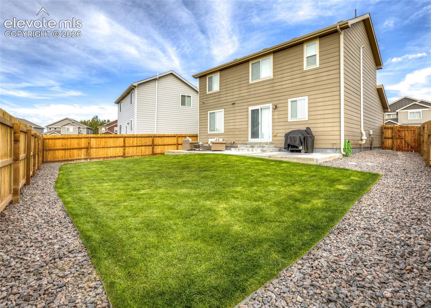 Rear exterior featuring horizontal lap siding, a concrete patio, a manicured lawn, and perimeter wood fencing with rock landscaping borders