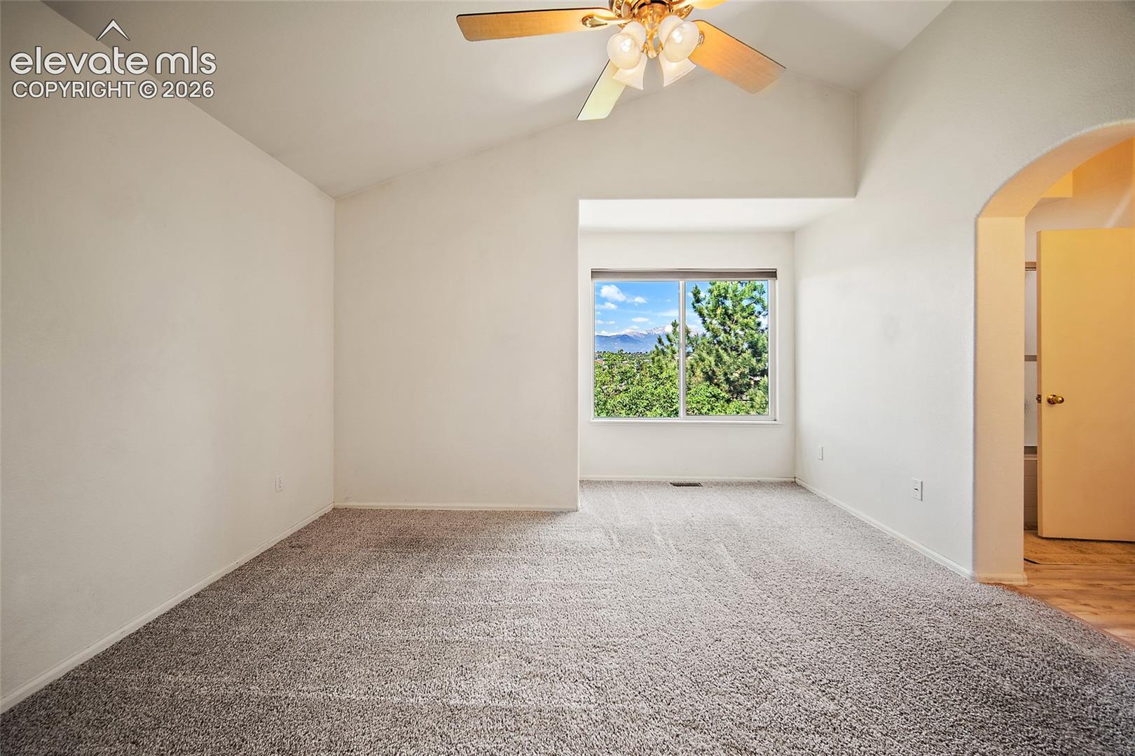 Carpeted room featuring a window with expansive outdoor scenery, a vaulted ceiling, a ceiling fan with integrated lighting, and an arched doorway opening to an adjacent space