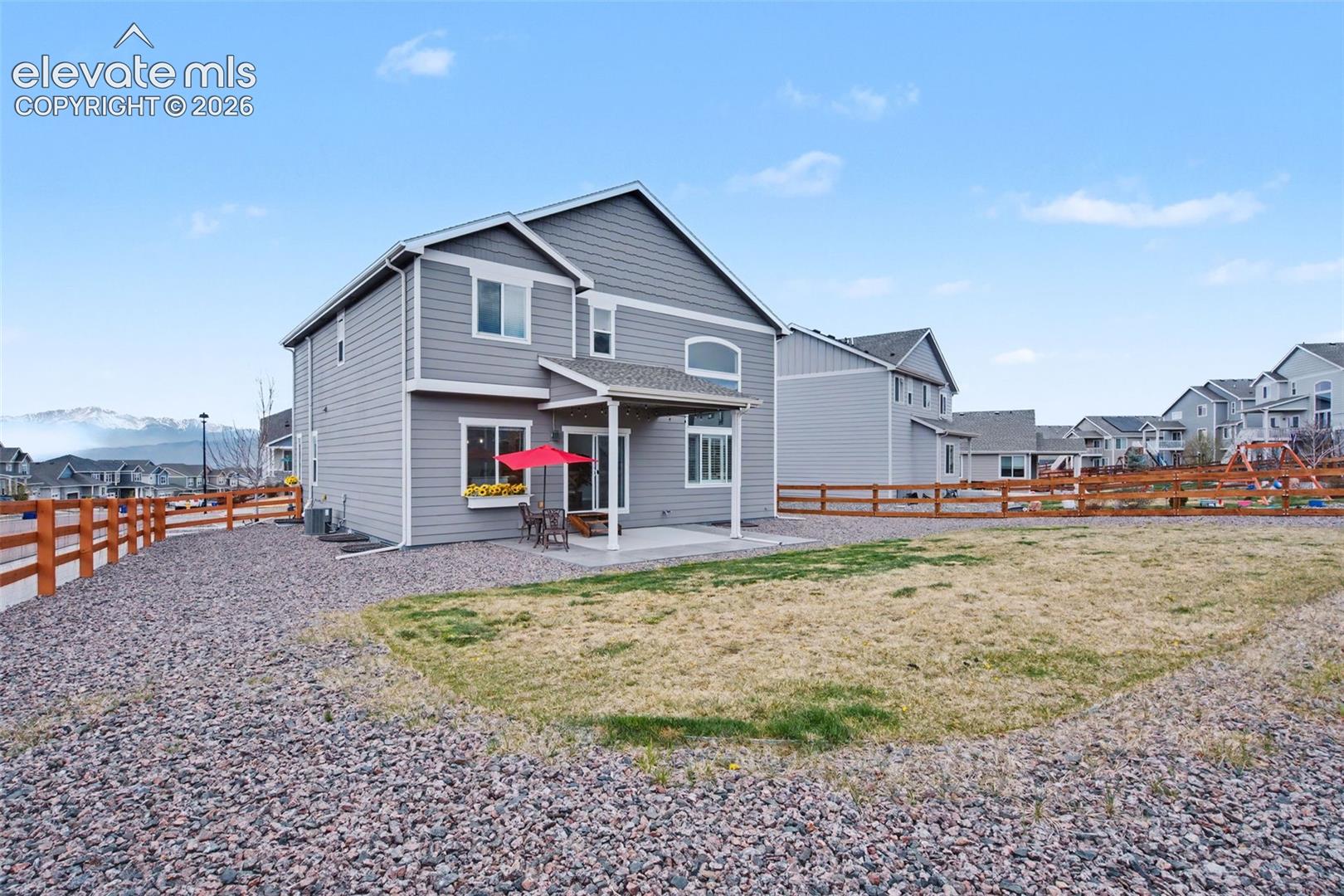 Two-story residence with gray siding, featuring a covered patio and an expansive gravel landscaping area