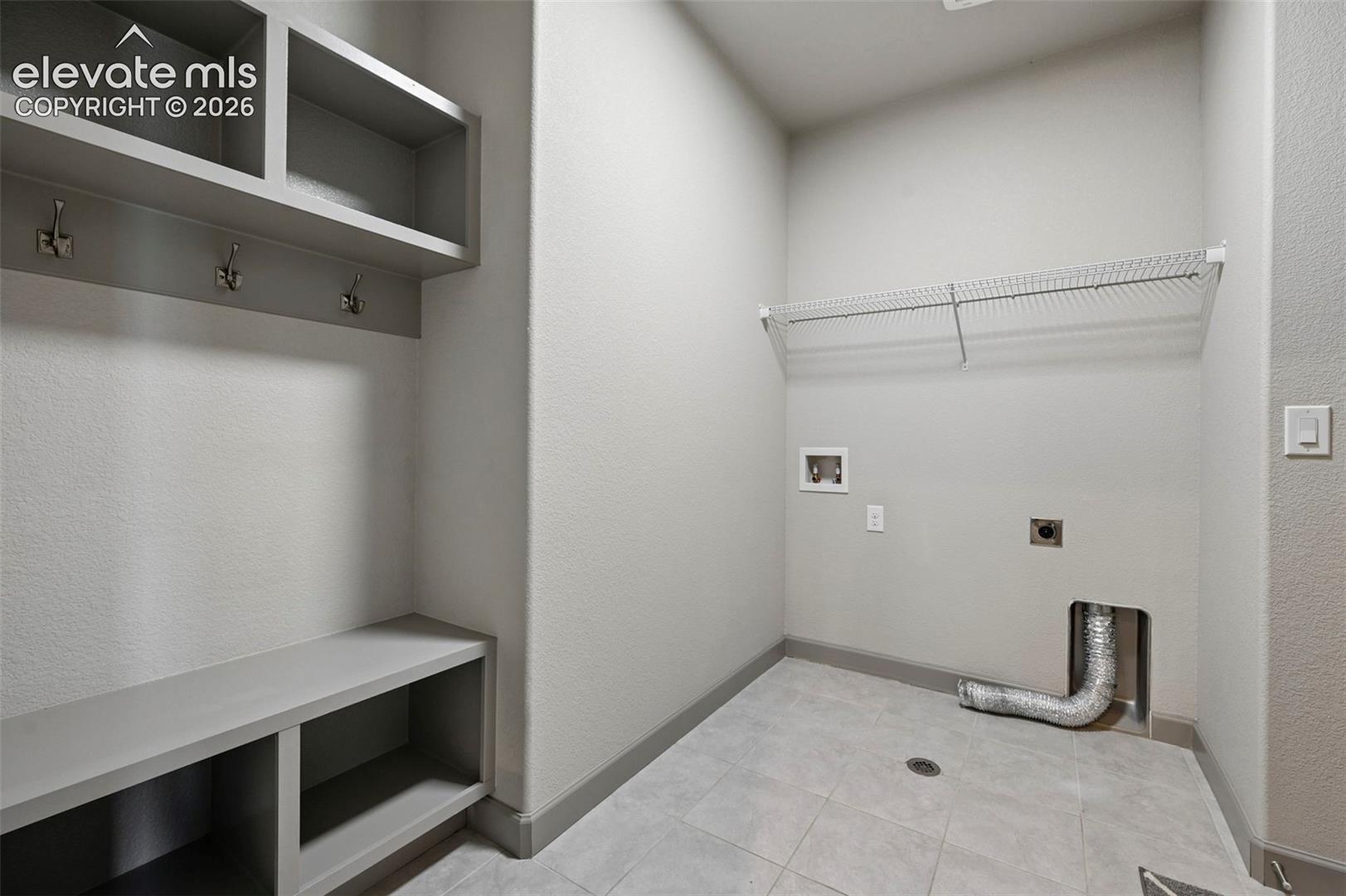 Utility area featuring built-in cabinetry with integrated bench seating, three metallic garment hooks, overhead shelving, and tile flooring