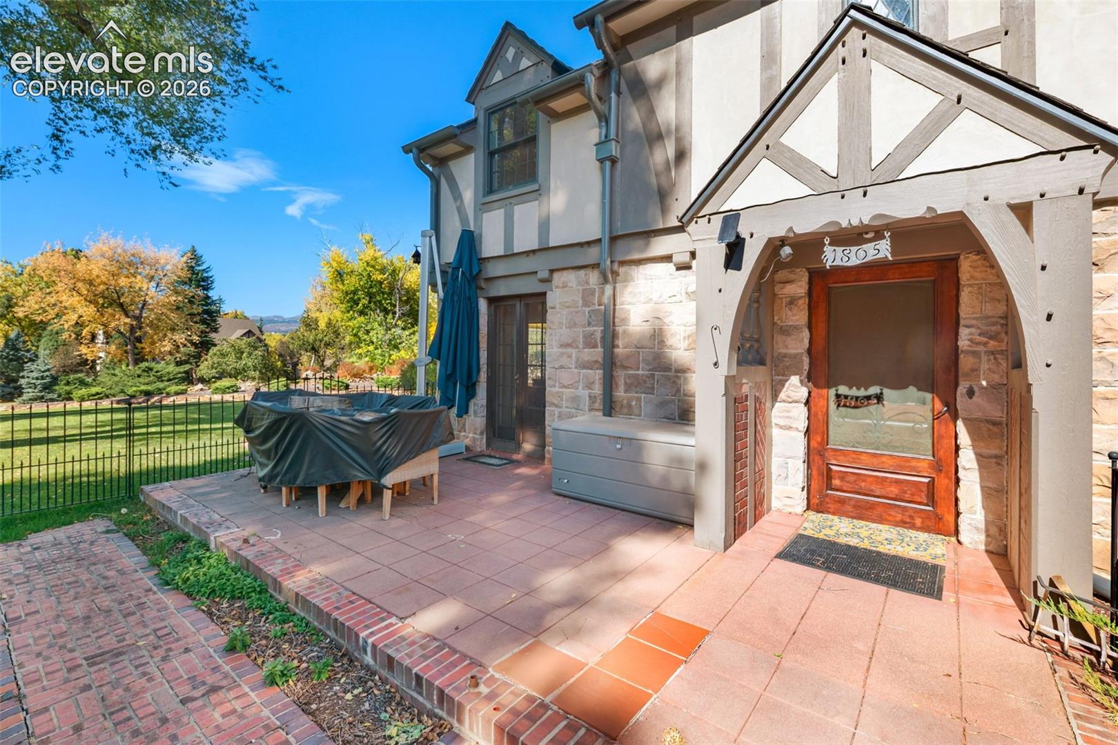 Tudor-style exterior featuring stone masonry, half-timbering, a covered entryway with a gabled porch, and a tiled patio