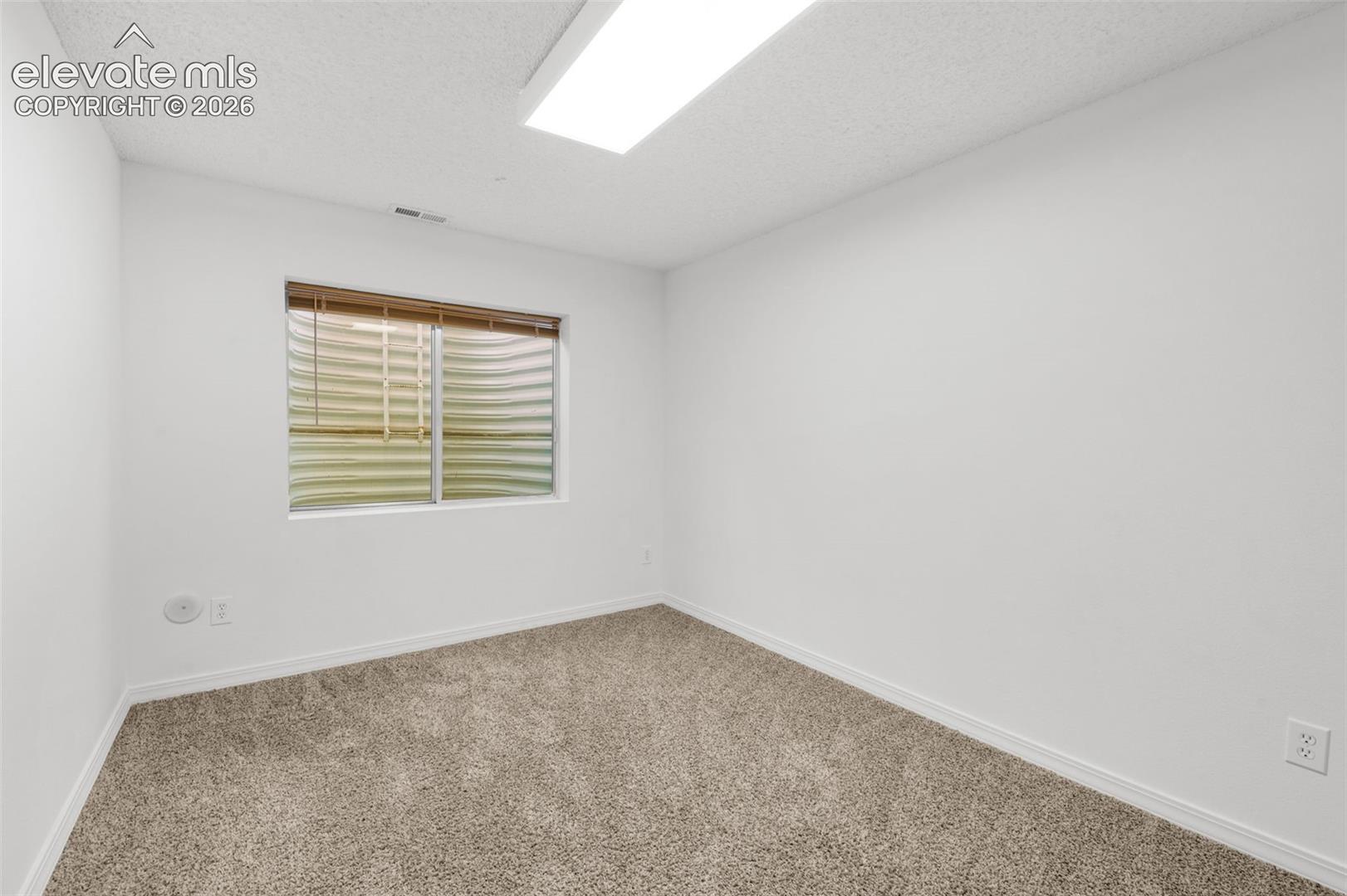 Neutral wall finishes, textured carpeting, and a single window with blinds