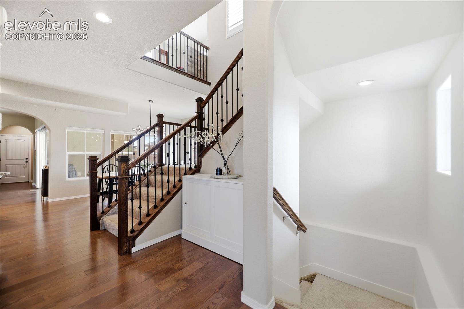 Expansive wood flooring, two-story entryway with staircase, wrought iron balusters, recessed lighting, and white trim