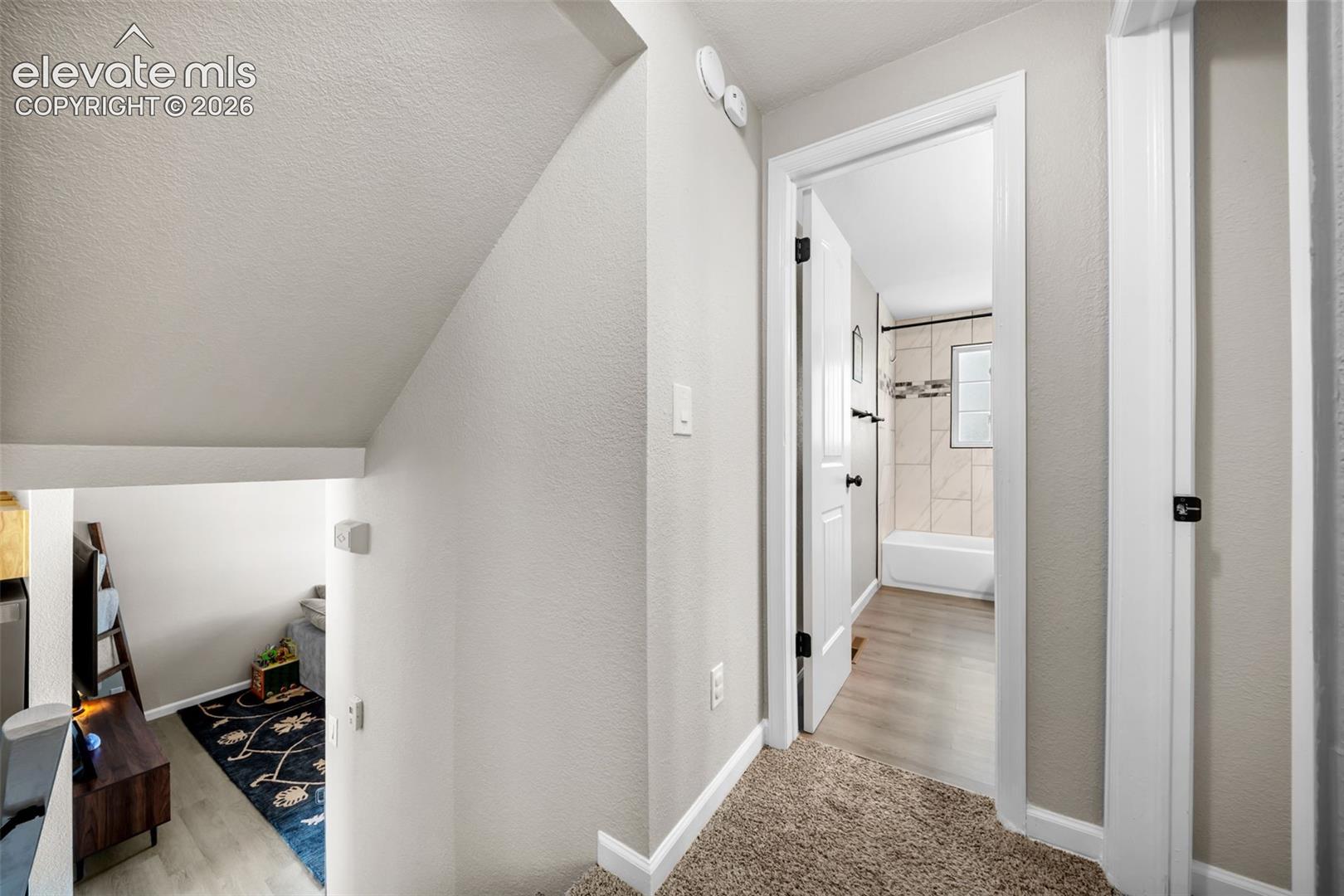 Doorway with white trim and dark hardware, leading to a bathroom featuring a tiled shower and window