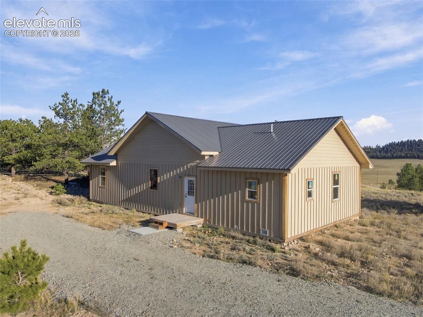 Single-story residence featuring vertical board-and-batten siding, a metal roof, and a gravel driveway