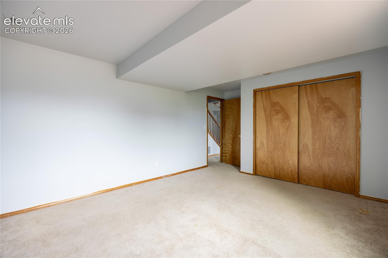 Carpeted flooring, light wood-tone baseboards, light-toned walls, wood-tone sliding closet doors, and a wood-tone entry door
