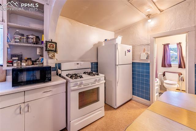 Kitchen with white appliances, light countertops, tile walls, open shelves, and white cabinets