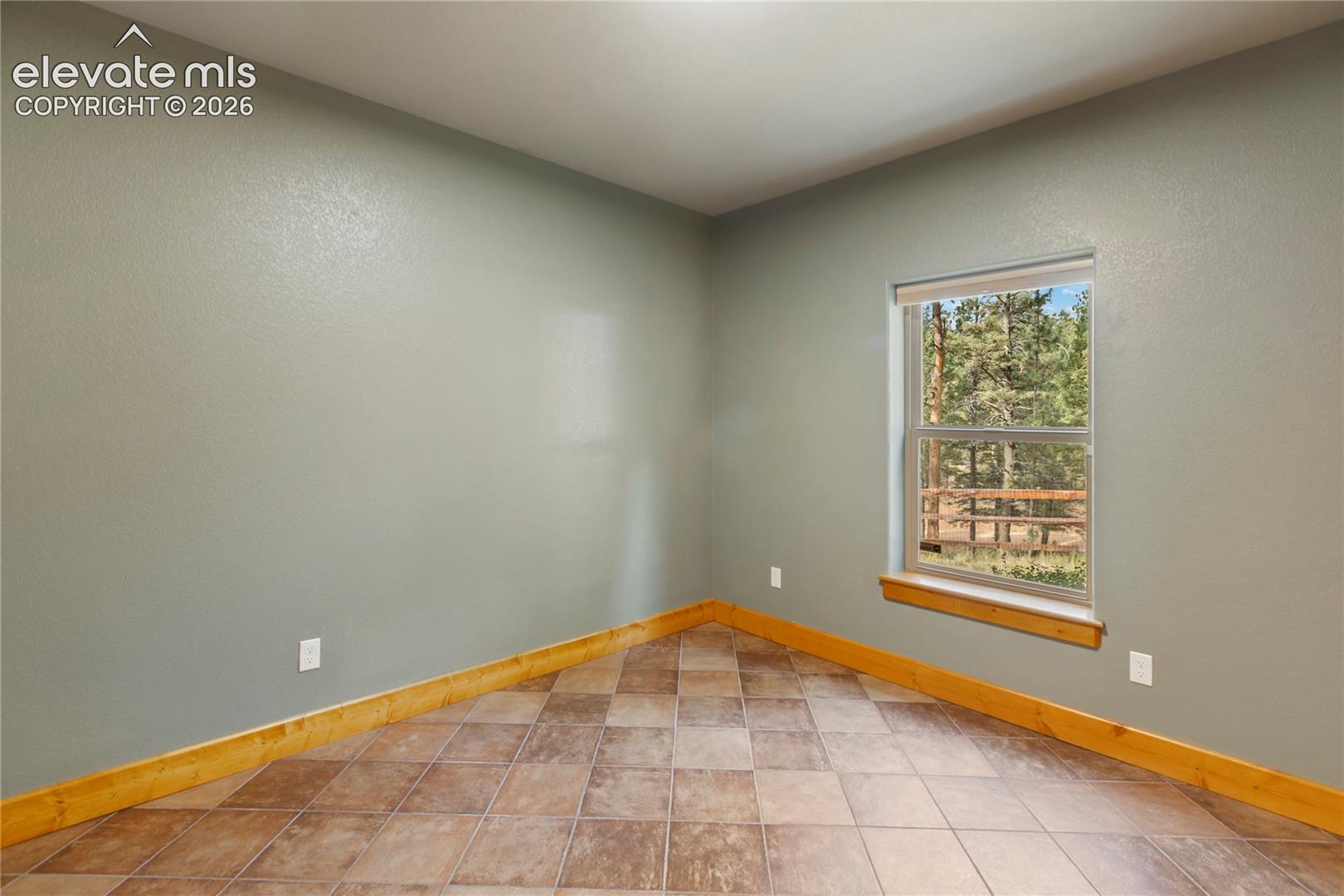 Neutral-toned interior walls featuring polished tile flooring, natural wood trim, and a window with exterior forest scenery