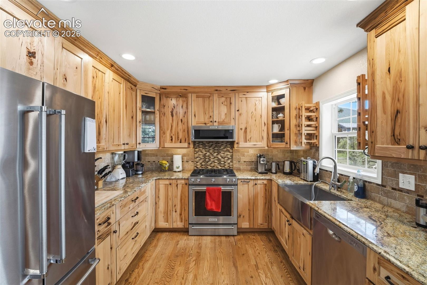 Kitchen featuring natural wood cabinetry, stainless steel appliances, granite countertops, a stone tile backsplash, and wood-finish flooring