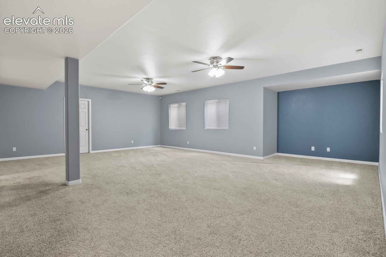 Spacious room featuring neutral carpeting, light blue wall paint, and multiple ceiling fans