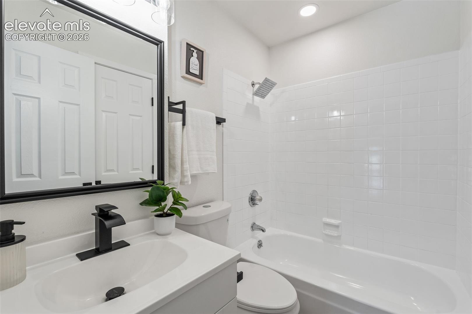 Bathroom featuring a vanity with a white countertop and basin, matte black faucet, wall-mounted mirror with a black frame, and a tub with a white tiled surround