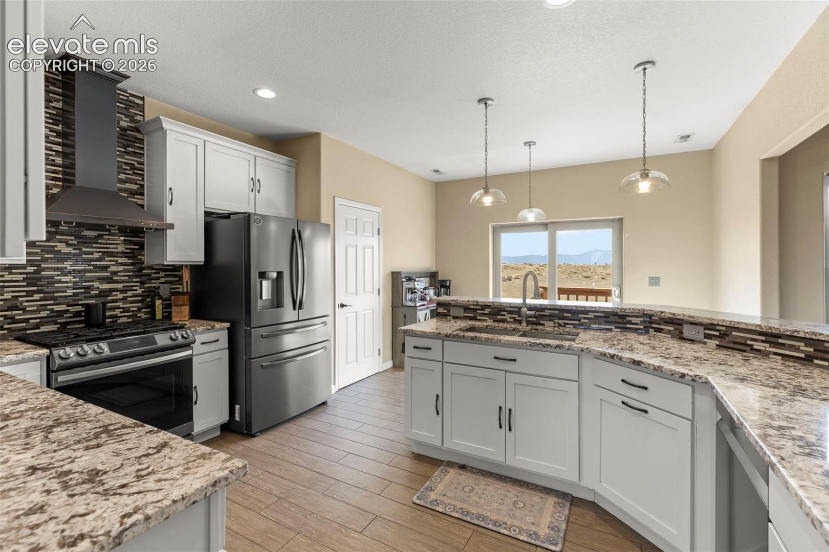 Kitchen featuring white shaker cabinetry, stone-patterned countertops, a tile backsplash, stainless steel appliances, and pendant lighting