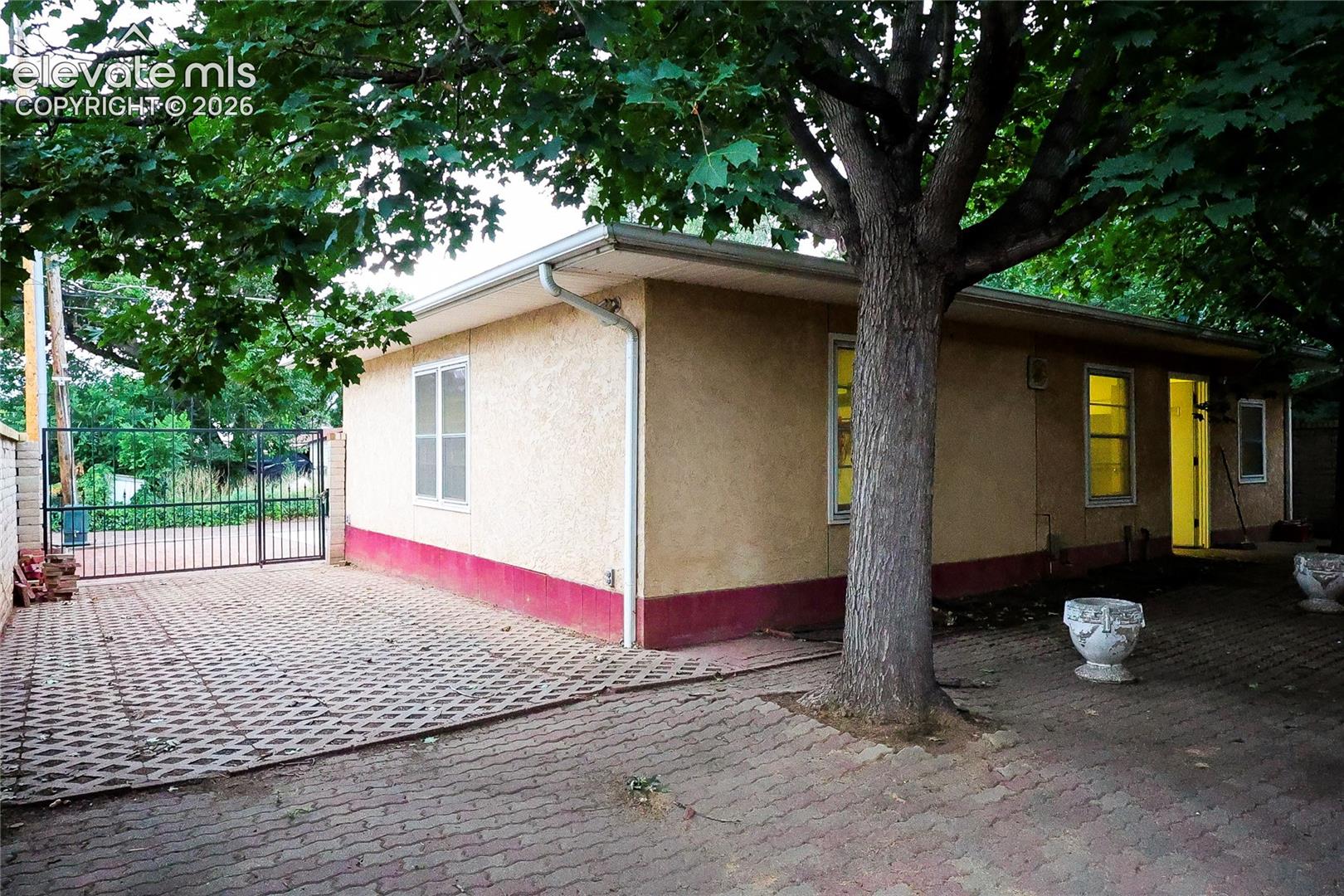 Stucco exterior with a contrasting lower band, white gutters, multiple windows, and a paved outdoor area