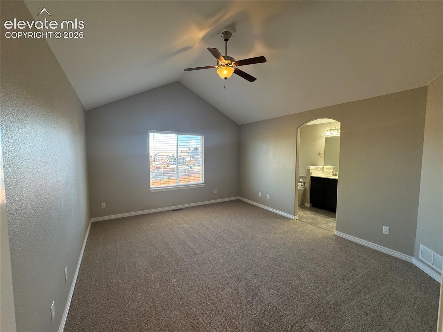 Vaulted ceiling, ceiling fan with integrated lighting, wall-to-wall carpeting, and an arched entryway