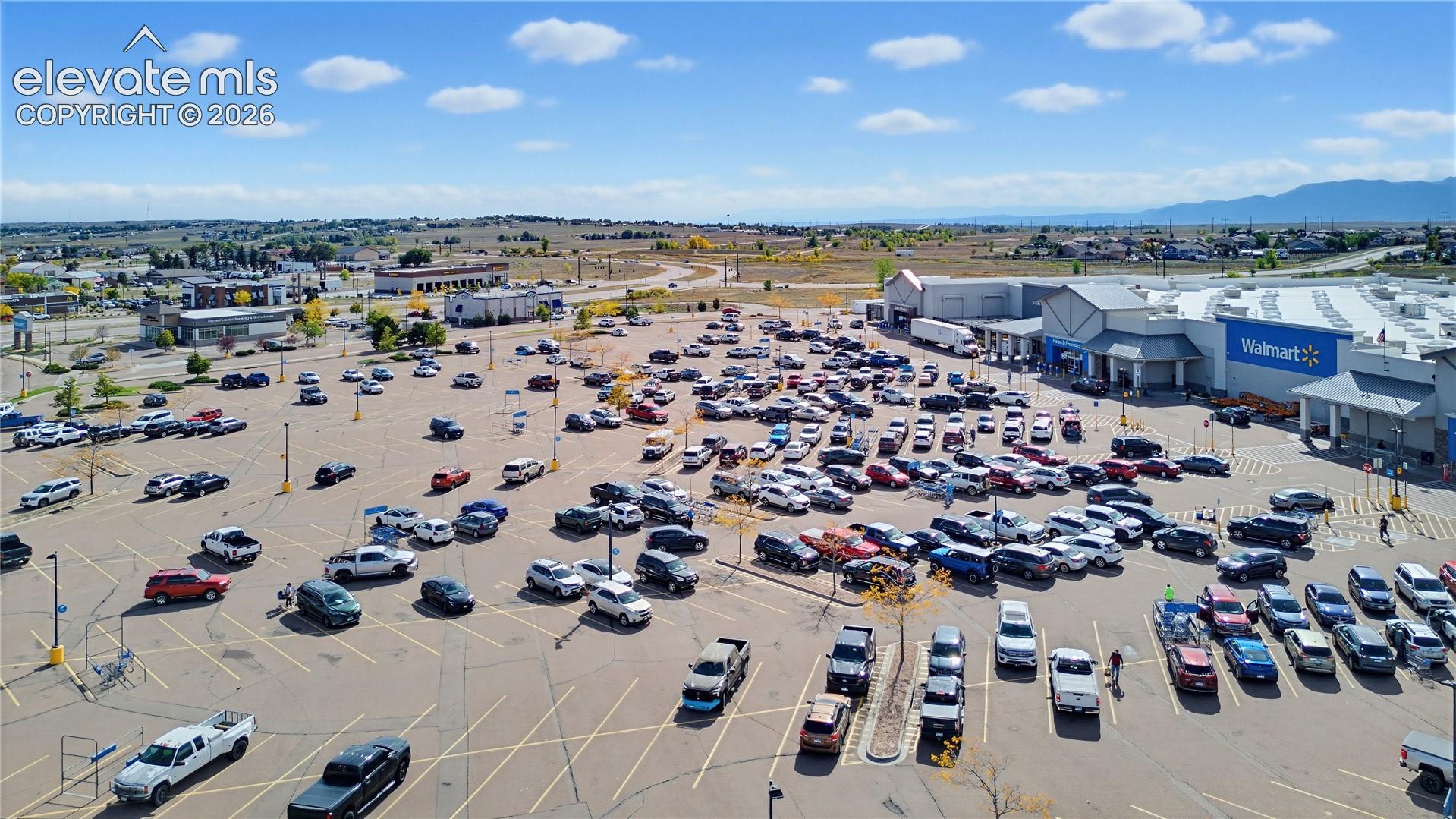 Aerial perspective showcasing a large-scale commercial retail center with expansive paved parking facilities and mountain range horizon