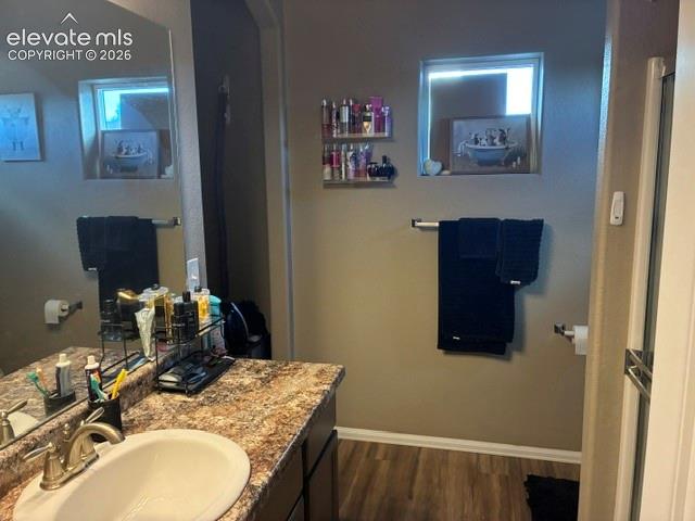 Bathroom featuring a large vanity with stone-patterned countertop, an undermount sink, brushed nickel faucet, wall-to-wall mirror, and wood-finish flooring