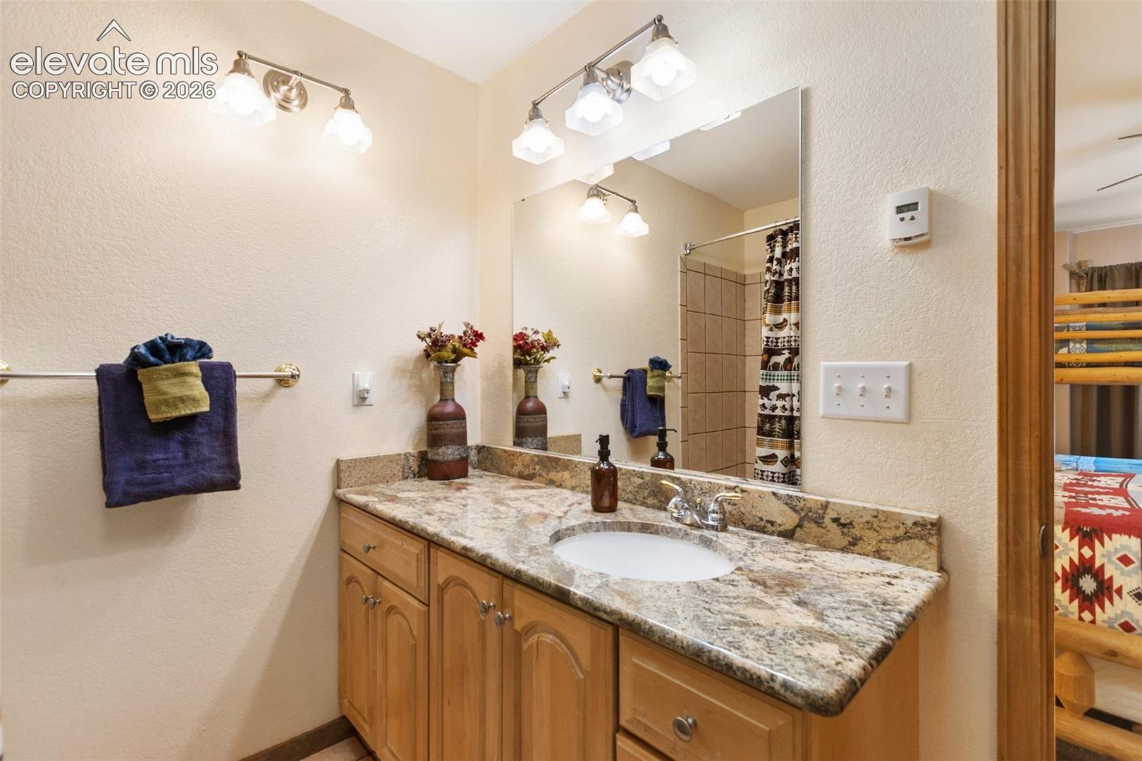 Vanity with light wood-finish cabinetry, stone countertop, undermount sink, and polished chrome faucet