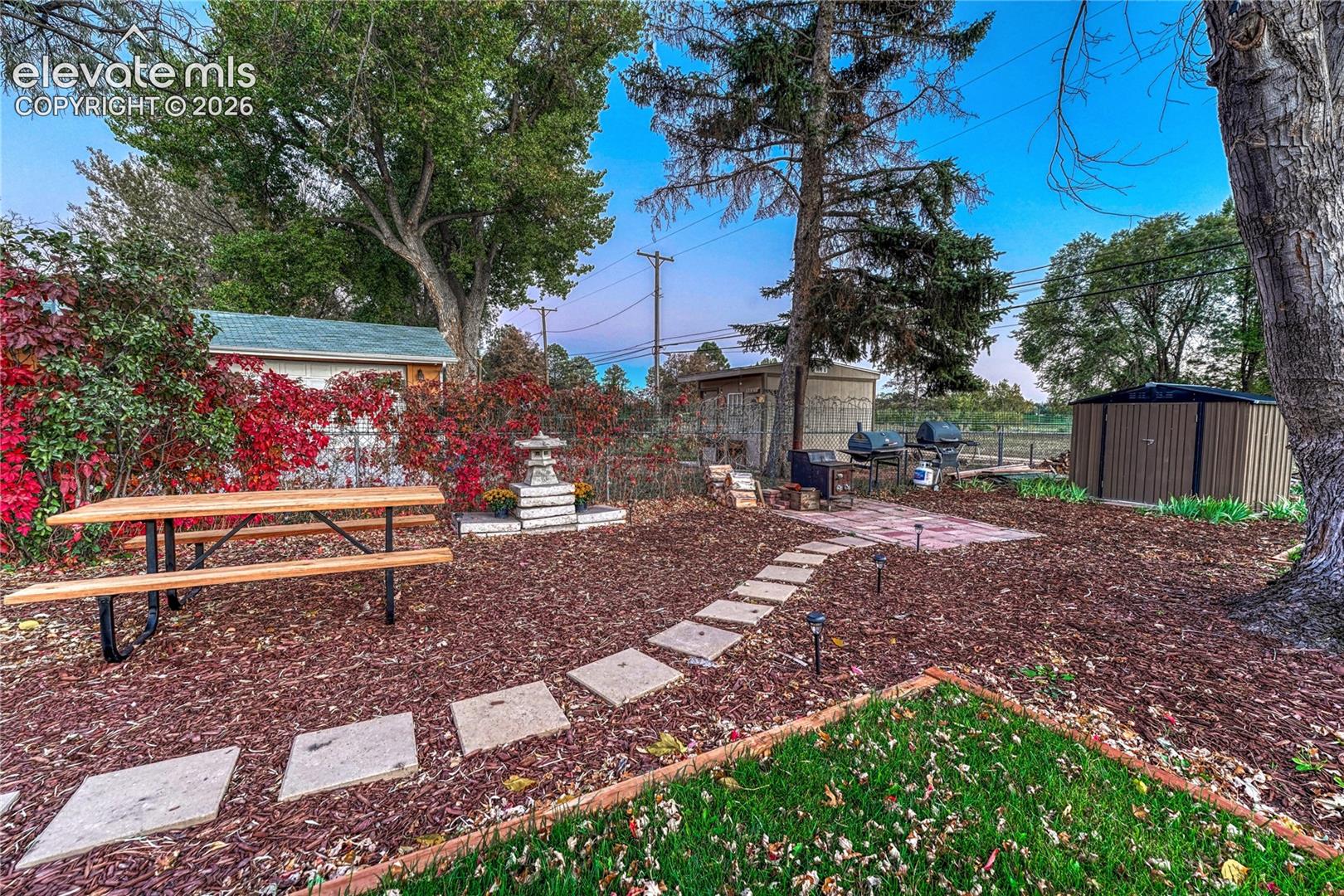 Backyard featuring a stone paver path, mature trees, mulch ground cover, and detached storage unit