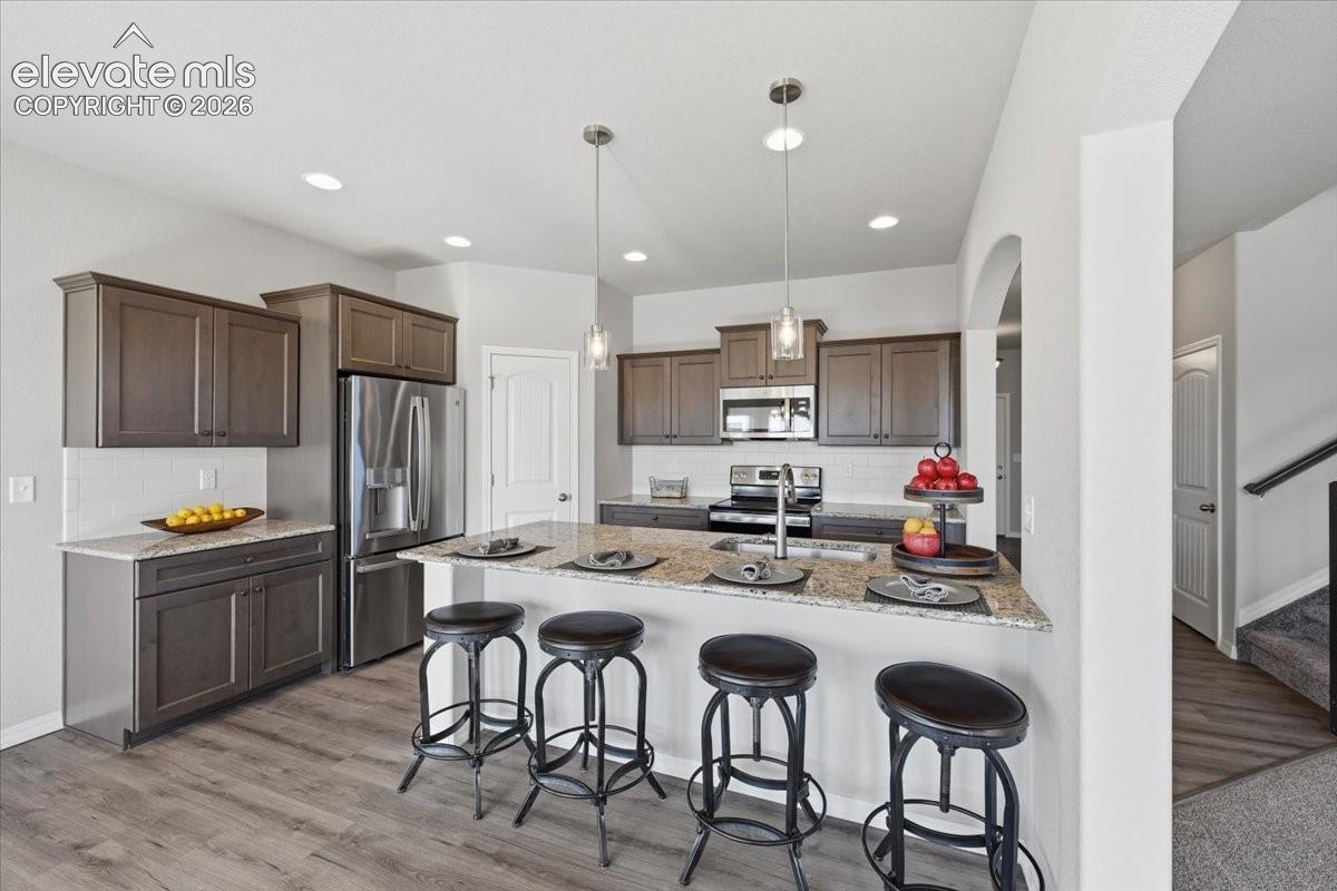 Kitchen featuring wood-finish cabinetry, stone-surface countertops, stainless steel appliances, recessed ceiling lighting, and dual glass-shade pendant lights over a breakfast bar