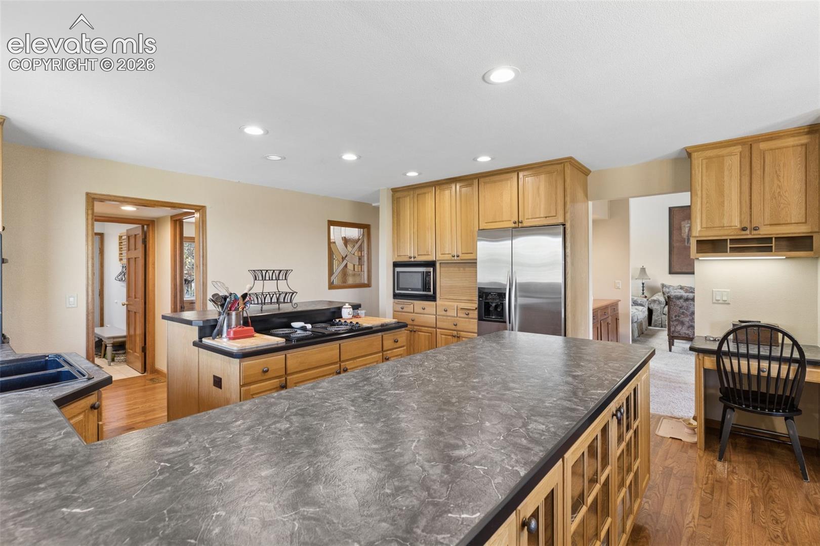 Kitchen featuring natural wood cabinetry, dark stone-finish countertops, stainless steel appliances, integrated desk space, and recessed lighting