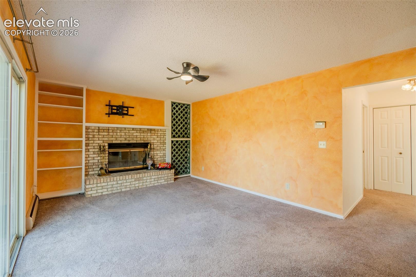 Built-in shelving, brick fireplace with a hearth, ceiling fan, and sliding glass door