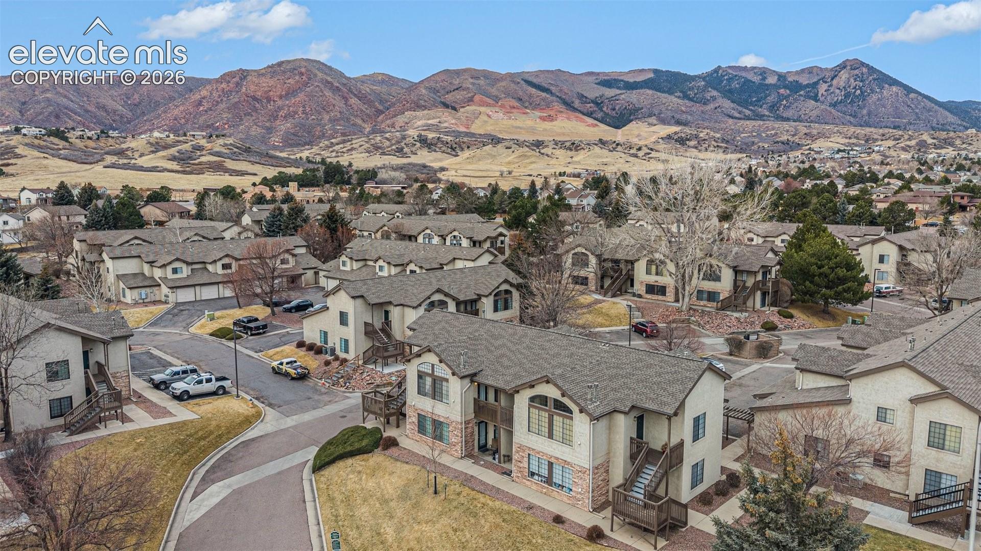 Aerial perspective featuring multi-story residential buildings with shingle roofing, exterior stucco and masonry facades, paved roadways, and mountain range backdrop