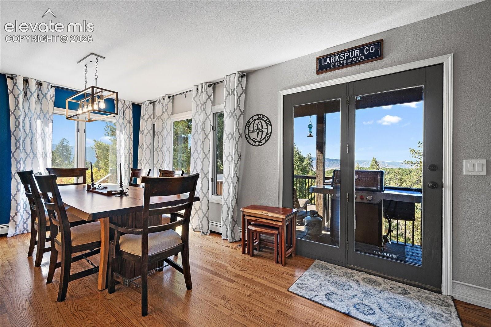 Dining space featuring wood-finish flooring, metal-framed pendant lighting, and double glass-paneled doors opening to an exterior deck