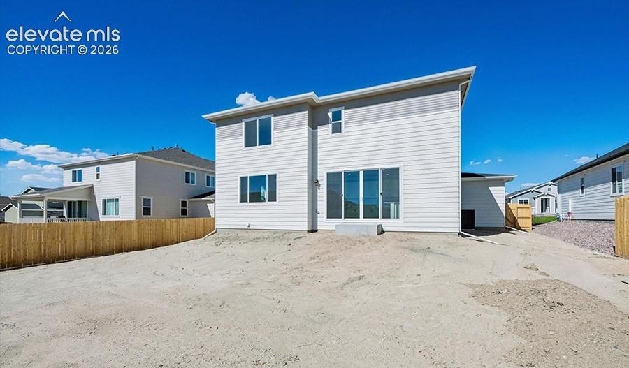 Two-story residential exterior featuring light-toned horizontal siding, a slanted roofline, sliding glass doors, and a wood privacy fence