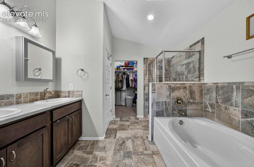 Bathroom featuring a double vanity with dark wood-finish cabinetry, a framed mirror, a built-in tub, a glass-enclosed shower, and tile flooring