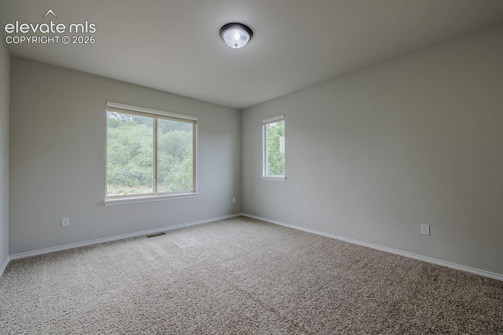 Bright and spacious bedroom featuring neutral carpeting, recessed ceiling lighting, and dual windows with natural light