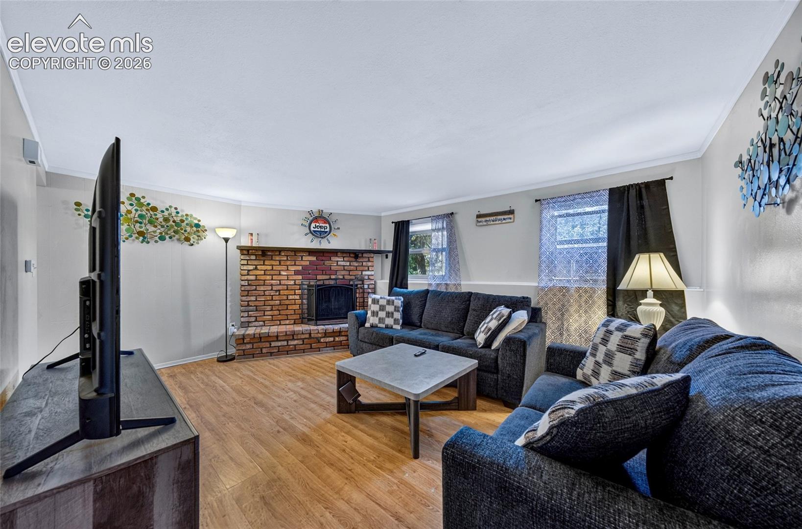 Living room featuring wood-finish flooring, a floor-to-ceiling brick hearth, and a fireplace with a masonry surround