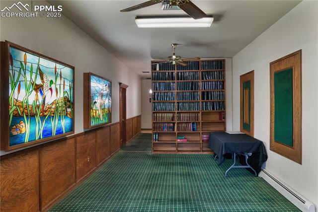 Sitting room with a baseboard heating unit, carpet floors, a wainscoted wall, and a ceiling fan