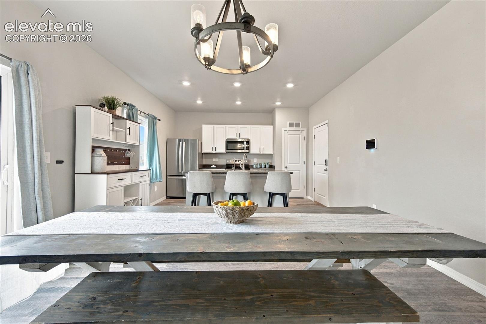 Kitchen featuring white cabinetry, stainless steel appliances, a center island with bar seating, and a decorative circular chandelier