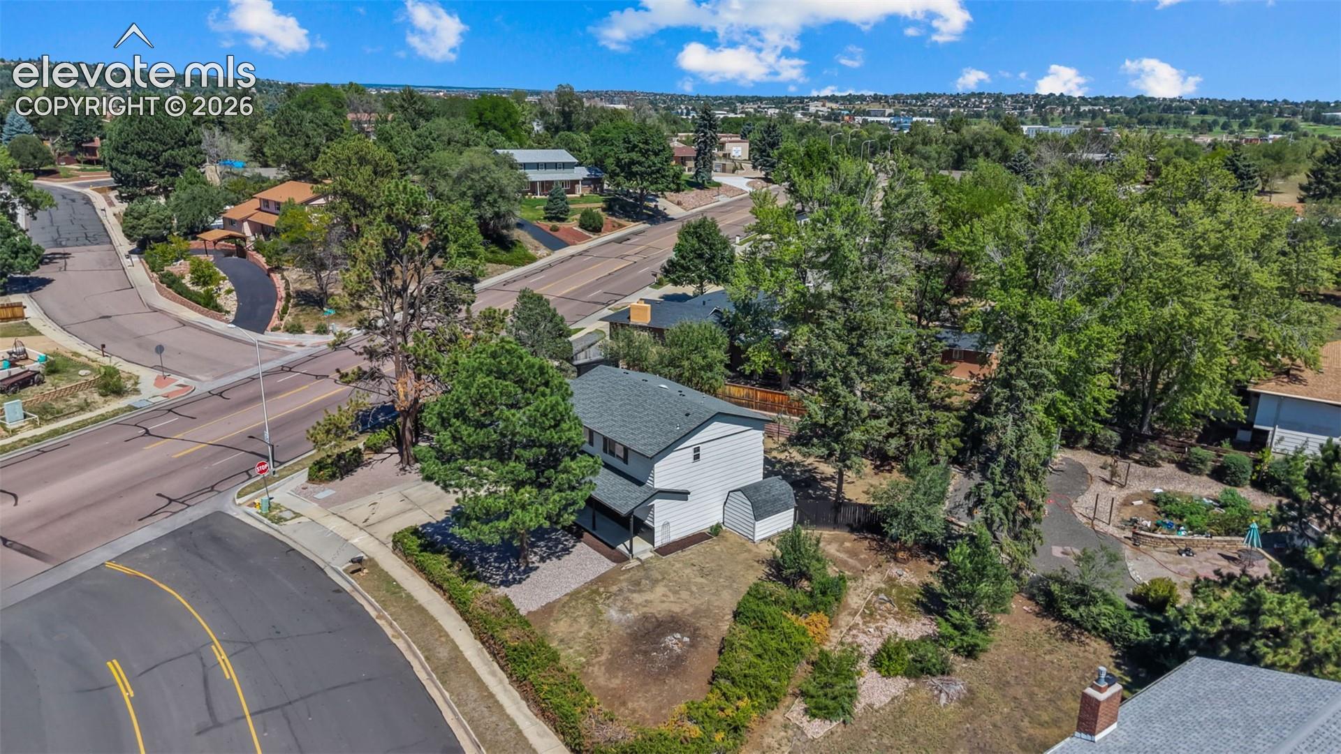 Two-story residence with a gray shingle roof, mature trees, and an attached storage shed