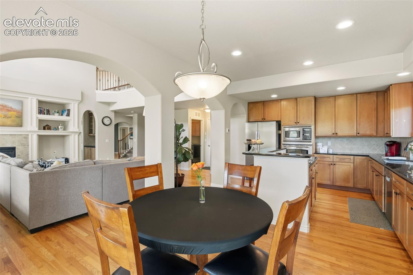 Open-concept kitchen featuring wood cabinetry, stainless steel appliances, and a black countertop island